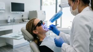 Odontóloga aplicando gel blanqueador con lámpara LED a una paciente en la clínica dental